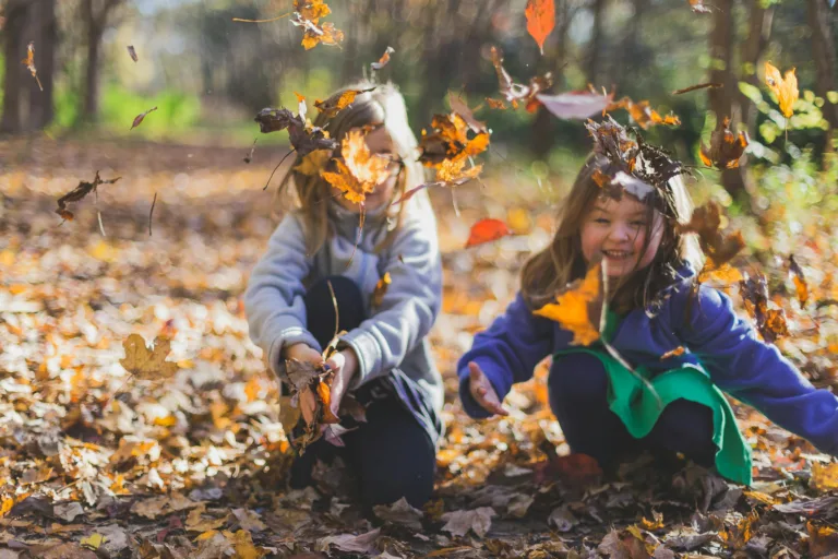 Reggio Emilia Approach & Nature-based Education 7 Two smiling girls playing joyfully amidst colorful fall leaves in a sunlit forest